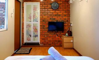 a small bedroom with a brick wall , a television mounted on the wall , and a bed with two towels at Petak Padin Cottage by The Pool, Kepala Batas Penang