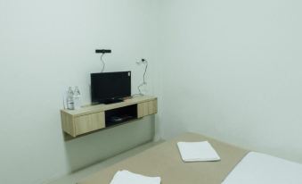 a small , white room with a television on a wooden shelf above the bed , along with two chairs placed nearby at Cheaper Room