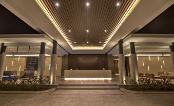 a modern hotel lobby with a reception desk , seating area , and potted plants under a ceiling with lights at Mambruk Hotel & Convention