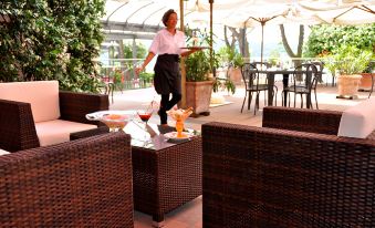 a woman in a black dress and white shirt is carrying a tray of food on her shoulder , while standing next to an outdoor patio with wicker at Hotel Marina