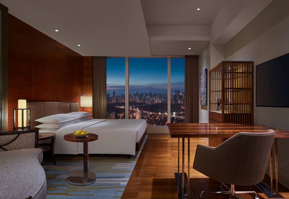 a modern hotel room with a large window offering a view of the city , white beds , wooden floors , and a dining table at Grand Hyatt Manila