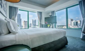 a large bed with white linens is in a room with windows overlooking a cityscape at Z Hotel