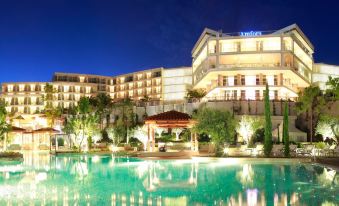 a large hotel with a swimming pool in front of it , surrounded by palm trees at Amfora Hvar Grand Beach Resort