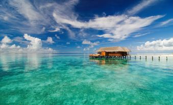 a tropical beach with a hut on stilts , surrounded by clear blue water and lush greenery at Mirihi Island Resort