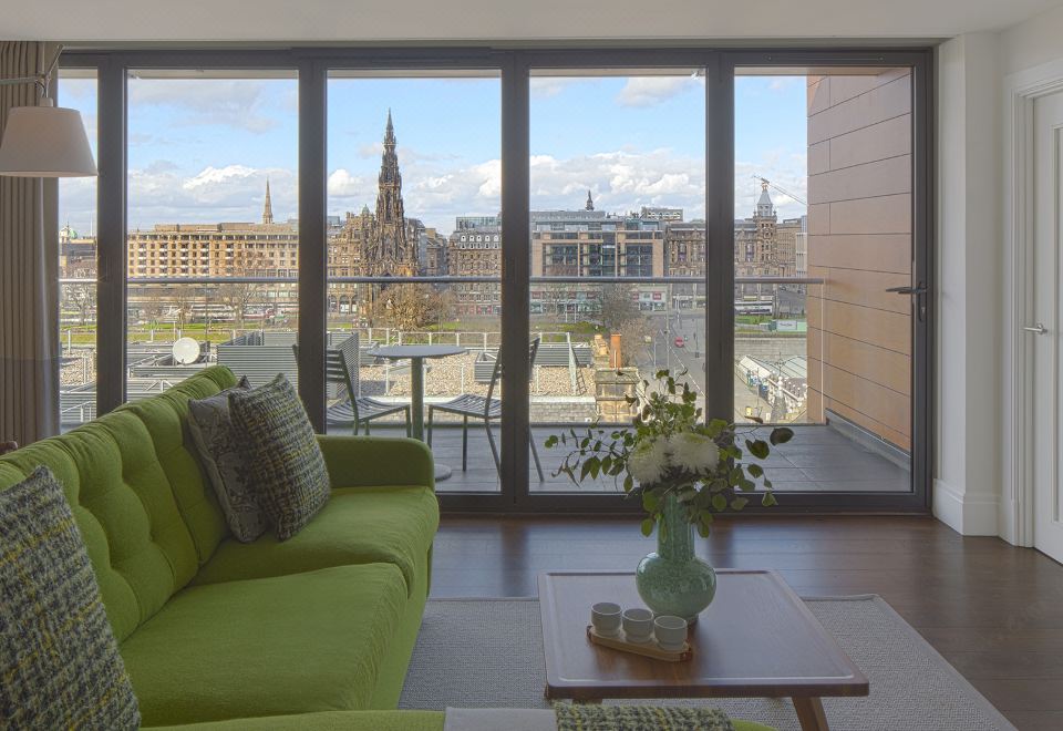 a living room with a green couch , wooden table , and large window offering a view of the city at Cheval Old Town Chambers