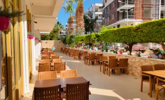 a restaurant with wooden tables and chairs , surrounded by palm trees and a large building at Altinersan Hotel
