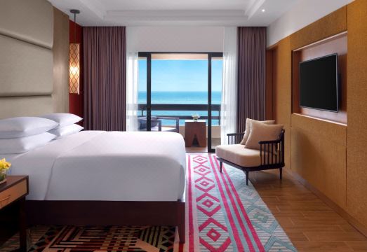 a modern hotel room with a large window offering a view of the ocean , white bedding , and wooden flooring , as well as comfortable furniture at Hyatt Regency Kuantan Resort