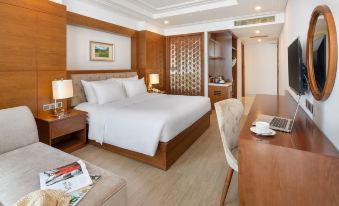 a hotel room with a king - sized bed , a laptop on the nightstand , and a comfortable couch at Paris Deli Danang Beach Hotel