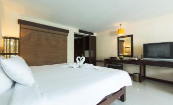 a large bed with white linens and a wooden headboard is in a room with a desk , television , and sink at Pattawia Resort & Spa, Pranburi