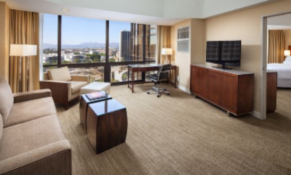 a modern living room with a large window offering a city view , including a desk , couch , and dining table at The Westin Bonaventure Hotel & Suites, Los Angeles