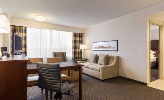 a modern living room with a beige couch , black chairs , and wooden tables , along with a large window and a cityscape painting on the wall at Embassy Suites by Hilton Baltimore at BWI Airport