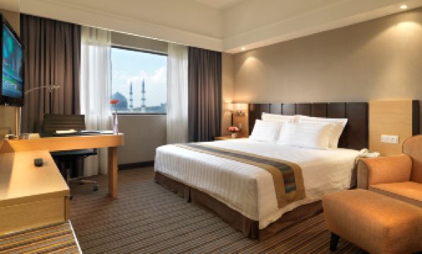 a hotel room with a king - sized bed , a desk , a chair , and a window overlooking the city at Concorde Hotel Shah Alam