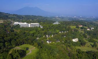 a large hotel complex surrounded by lush green trees and mountains , with a scenic view of the surrounding area at Royal Tulip Golf Resort Gunung Geulis
