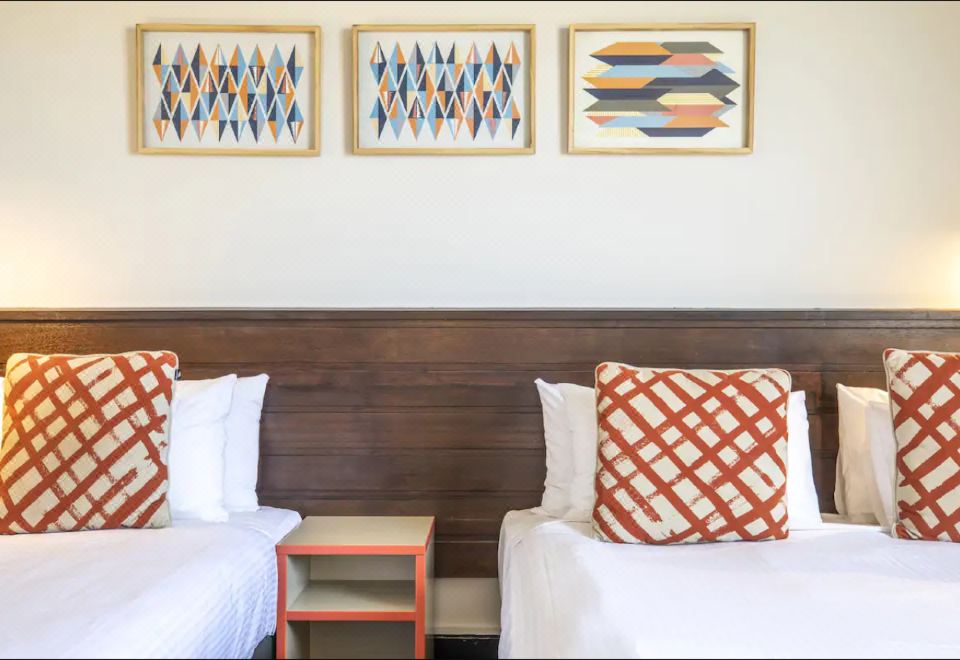 a hotel room with two beds , each topped with white sheets and orange and white patterned pillows , flanked by two nightstands at Nightcap at Glengala Hotel