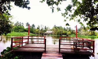 a wooden bridge spanning a body of water , surrounded by lush greenery and trees , providing a serene outdoor setting at Parn Dhevi Riverside Resort & Spa