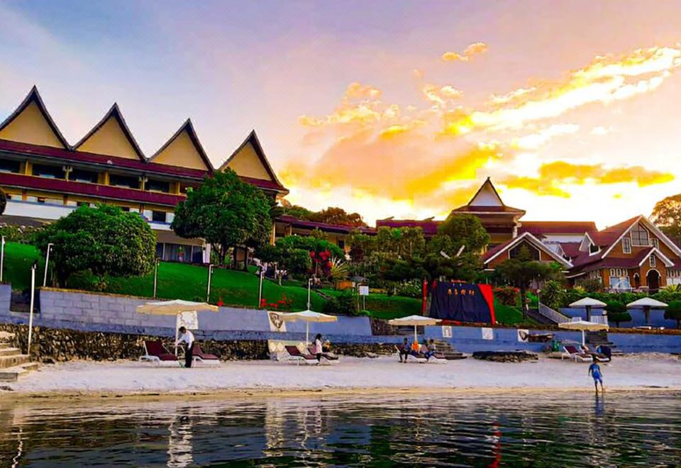 a beach with umbrellas and sun loungers on the sand , as well as a resort in the background at Khas Parapat