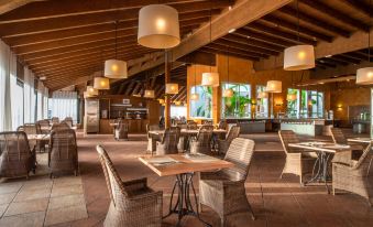 an indoor restaurant with wooden tables and chairs , hanging lamps , and a bar area in the background at Landmar Costa Los Gigantes