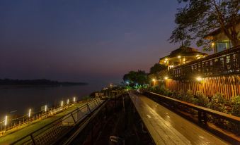 a wooden boardwalk with lights on , leading to a lit - up building near the water at night at Chiangkhan River Mountain Resort