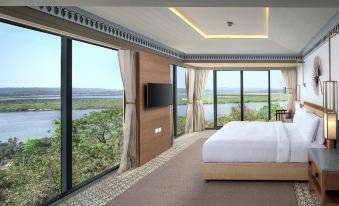 a large bed with a wooden headboard is in a room with large windows overlooking water at DoubleTree by Hilton Goa - Panaji