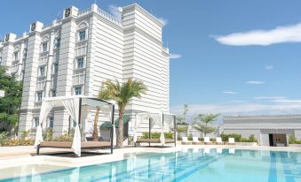 a large white building with a swimming pool in front of it , surrounded by palm trees at The Monarch Hotel