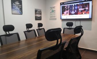a conference room with a large wooden table , black chairs , and a tv mounted on the wall at Monaco Hotel Cyberjaya