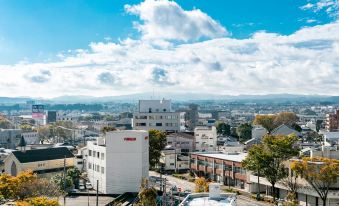 a city skyline with buildings and trees , under a blue sky dotted with clouds at Hotel Wing International Miyakonojo