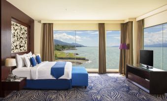 a luxurious bedroom with a large window overlooking the ocean , featuring a blue bed and a tv at Swiss-Belhotel Silae Palu