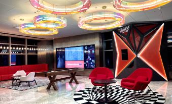 In the lobby, there are chairs and tables, and along the wall, there is an art piece at Radisson RED Hotel Zhuhai Gongbei Port