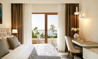 a luxurious hotel room with a large window offering a view of the ocean , a comfortable bed , and a desk at Potidea Palace Hotel