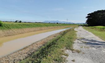 a dirt road is lined with a muddy bank and surrounded by green grass , trees , and mountains in the distance at Petak Padin Cottage by The Pool