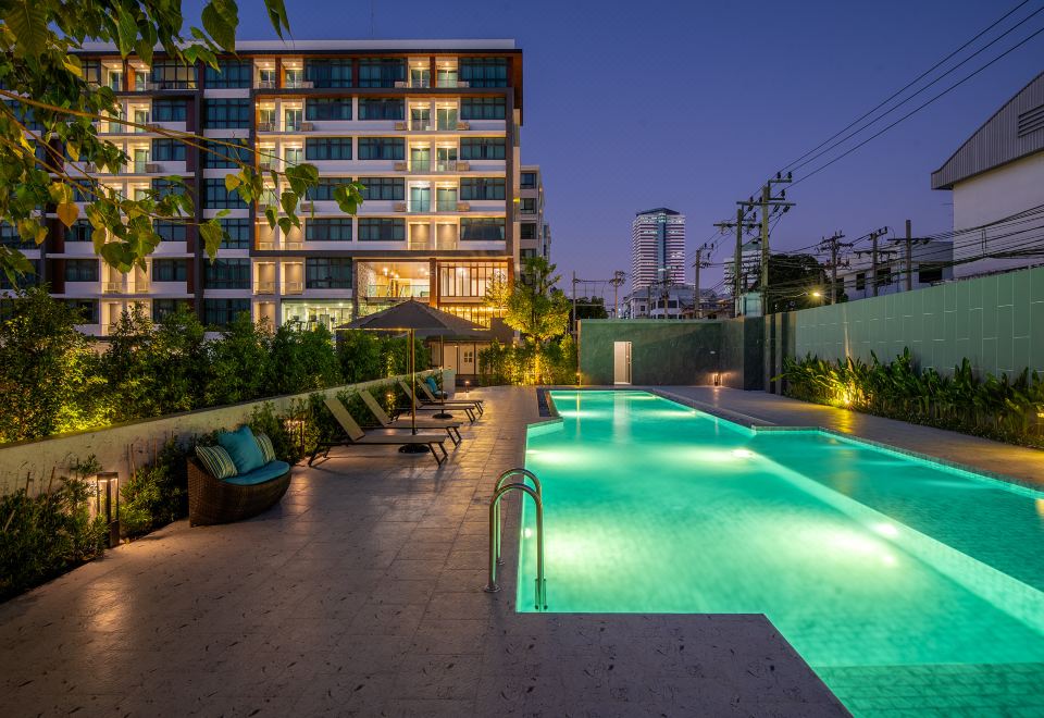 At night, there is a swimming pool in front of a building, with apartments and other buildings behind it at Orion Hotel & Residence