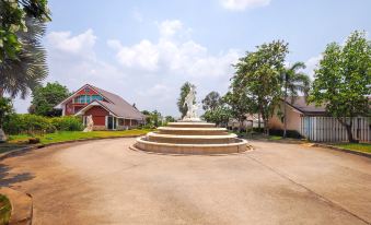 a fountain in the middle of a grassy field , surrounded by buildings and trees , with a clear blue sky overhead at OYO 926 Sydney Resort