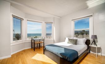 a bedroom with a bed , desk , and chairs is shown with a view of the ocean at Air Venice on the Beach