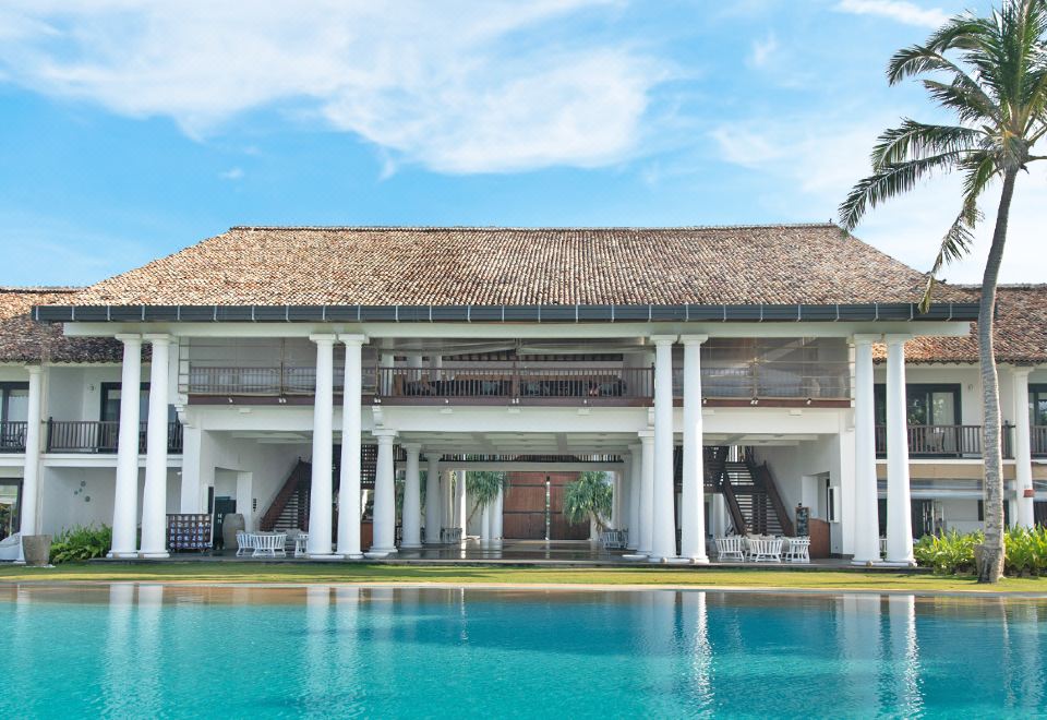 a large white building with a pool in front of it , surrounded by palm trees at The Fortress Resort & Spa