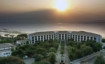 a large building with a parking lot in front of it and the sun setting behind the water at Haile Resort Hawassa