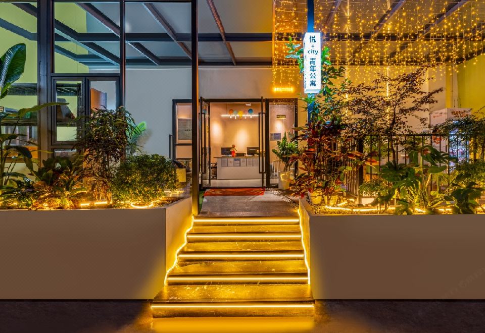 At night, a well-lit building entrance is adorned with decorative plants at Yue City Youth Apartment