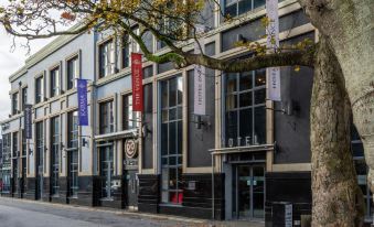 a modern building with a black exterior and red banners , situated on a street next to trees at The Prince of Wales Hotel