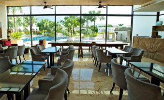 a modern restaurant with a large window offering a view of a swimming pool and palm trees at J Resort