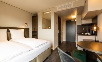 a modern hotel room with a bed , desk , and chair , as well as a kitchen area at Maseven München Messe Dornach