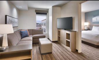 a living room with a couch , ottoman , and television is shown next to a window at Hyatt House Provo/Pleasant Grove