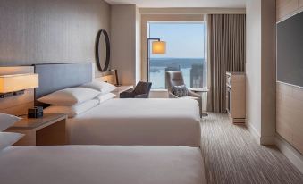 a hotel room with two beds , a chair , and a window overlooking the ocean through a glass door at Hyatt Regency Seattle