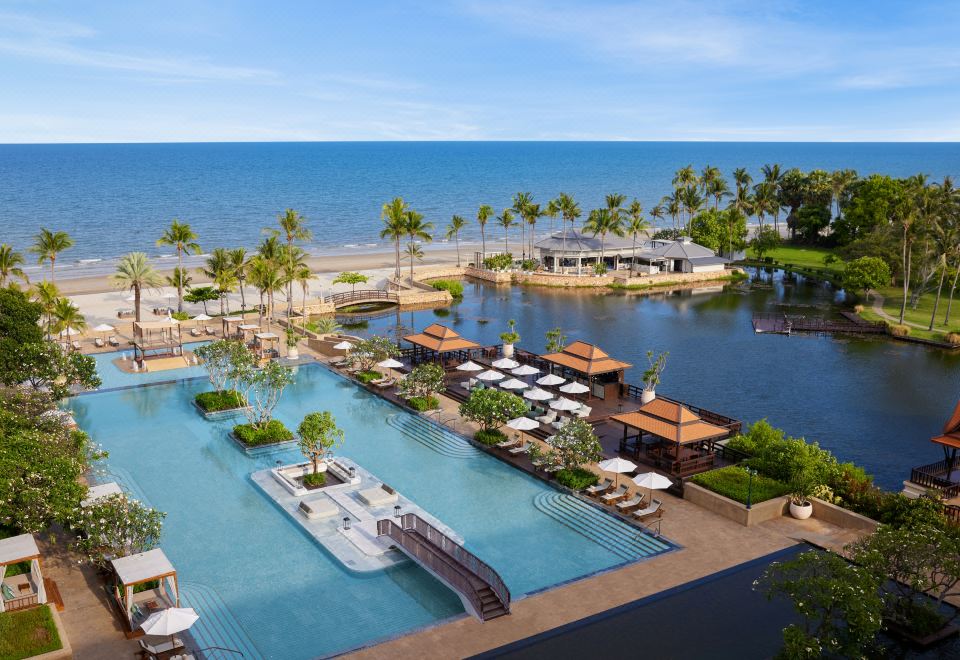 a large resort with a pool surrounded by palm trees and a body of water at Dusit Thani Hua Hin