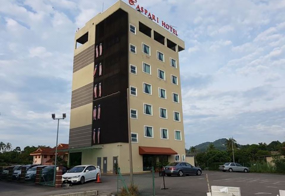 a tall hotel building situated in a parking lot , surrounded by trees and other structures at Caspari Hotel