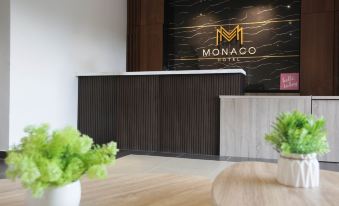 a modern hotel lobby with a wooden reception desk and a black marble wall displaying the monaco hotel logo at Monaco Hotel Cyberjaya