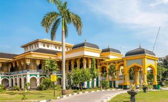 a large yellow building surrounded by palm trees , with a blue sky in the background at Alpha Inn