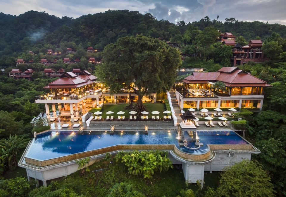 a large resort with a pool surrounded by lush greenery , including trees and bushes , as well as a hotel in the background at Pimalai Resort & Spa