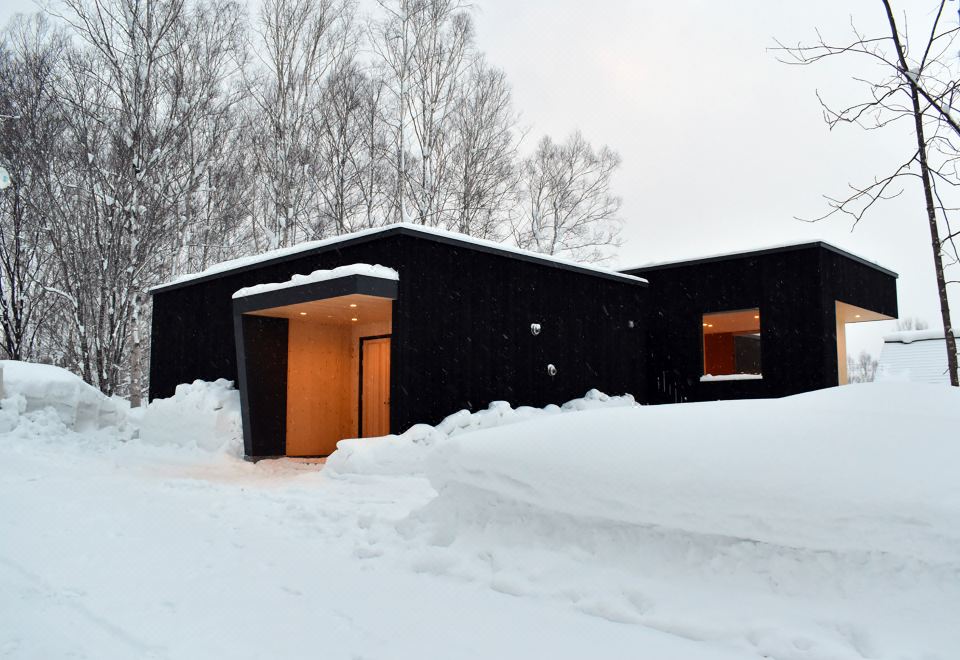 a black house with an orange door is nestled in the snow , surrounded by trees at Birchwood Chalet