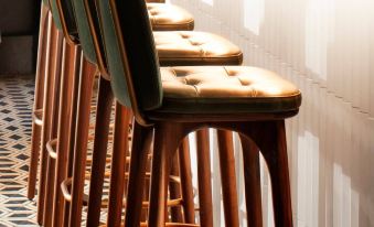 There is a row of stools and tables in the middle of the room, adjacent to an unoccupied bar area at The Hari Hong Kong