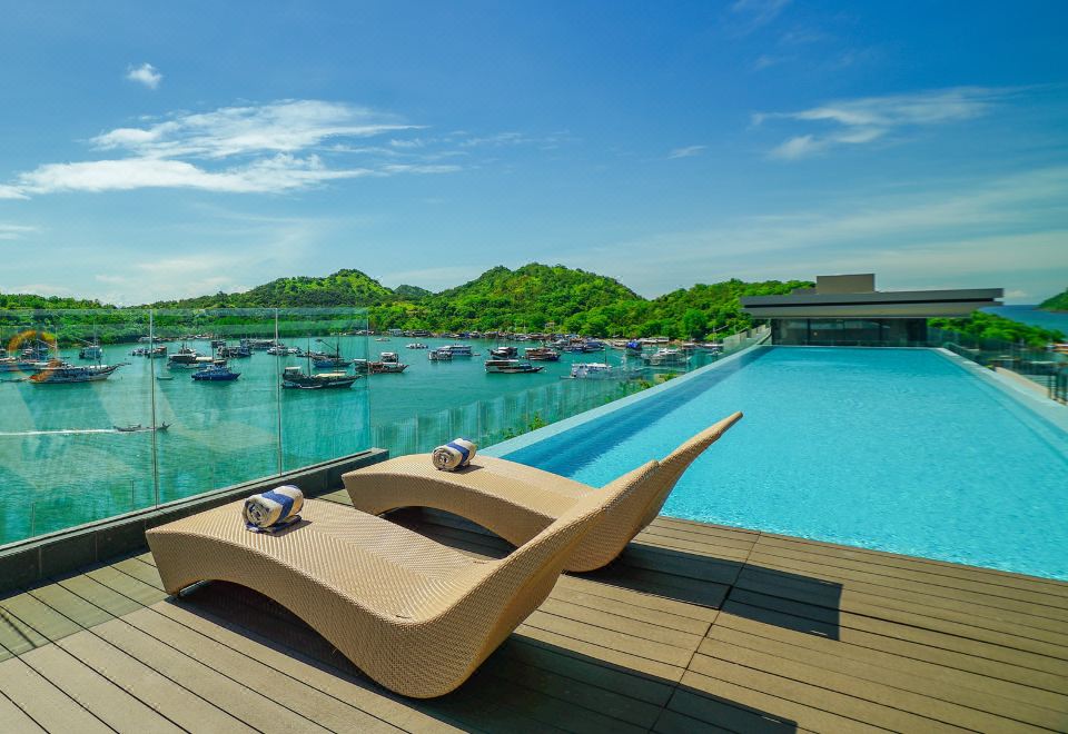 a wooden deck overlooking a pool , with several lounge chairs placed around the pool for relaxation at Meruorah Komodo Labuan Bajo