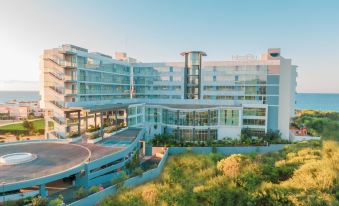 a modern , multi - story building with a curved design and large windows is surrounded by greenery at NissiBlu Beach Resort